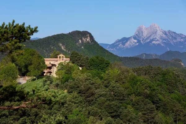 Una masia de pedra en un turó boscós amb el Pedraforca al fons