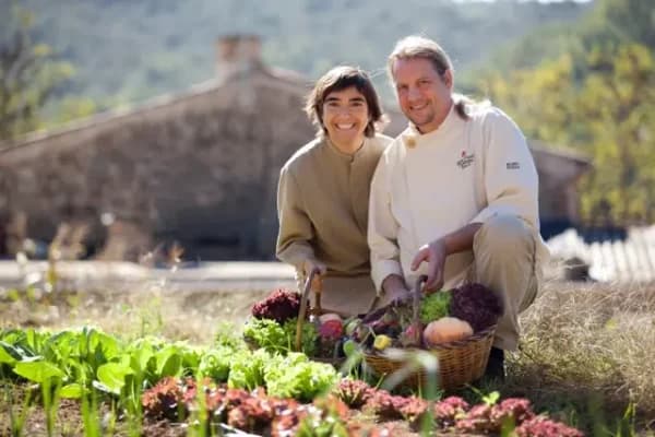 Dues persones somrient en un hort amb un cistell de verdures acabades de collir